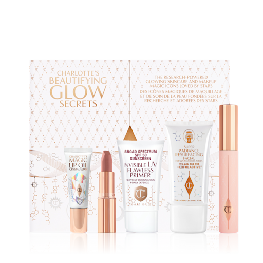 Charlotte's Beautifying Glow Secrets displayed Lip oil in a white-coloured tube with a gold-coloured lid, nude pink matte lipstick in gold-coloured tube, SPF-infused primer in a white-coloured tube, exfoliating wash-off mask in a white-coloured tube, mascara in pink-coloured tube with gold-coloured lid.