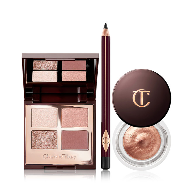 An open, mirrored-lid quad eyeshadow palette with beige, brown-gold, rose gold, and dusky pink shades, an eyeliner pencil in black, and cream eyeshadow in a coppery-gold shade in a glass pot with a dark brown-coloured lid. 