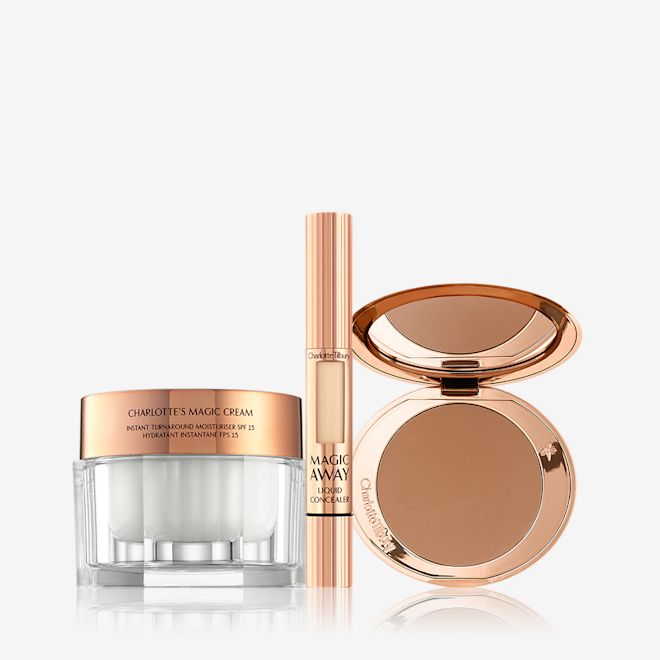 Magic Cream, Airbrush Bronzer, and Magic Away dispalyed An open, mirrored-lid bronzer compact in a medium-brown shade, a liquid concealer in a golden-coloured tube with a small window on the tube to view the shade inside, and pearly-white face cream in a glass jar with a golden-coloured lid.