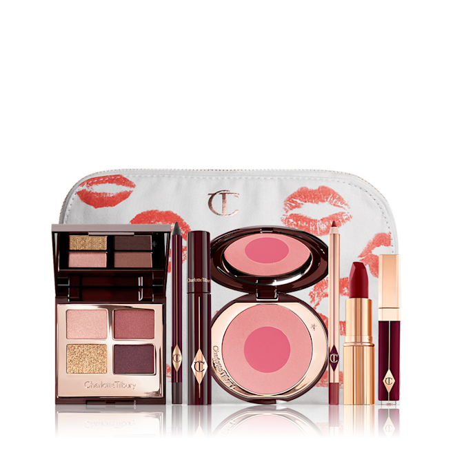 Vintage Vamp fair tone Makeup Kit & Complimentary Makeup Bag displayed A makeup bag with 7 makeup products, an open, mirrored-lid eyeshadow palette in matte and shimmery gold and red shades, an open black eyeliner pencil, a mascara in a dark-crimson colour scheme, a red lipstick with a matching lip liner pencil, vampy-red lip gloss, and an open two-tone blush in cool pink.