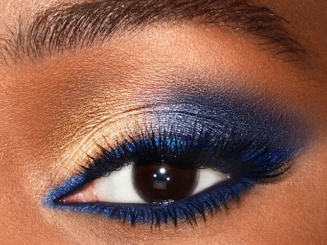 Super Blue look on deep tone model brown eye close-up Close-up of a deep-tone model's brown eye with shimmery gold and royal blue eyeshadow with matte and metallic eyeliner in royal blue on the upper eyelid and lower waterline.