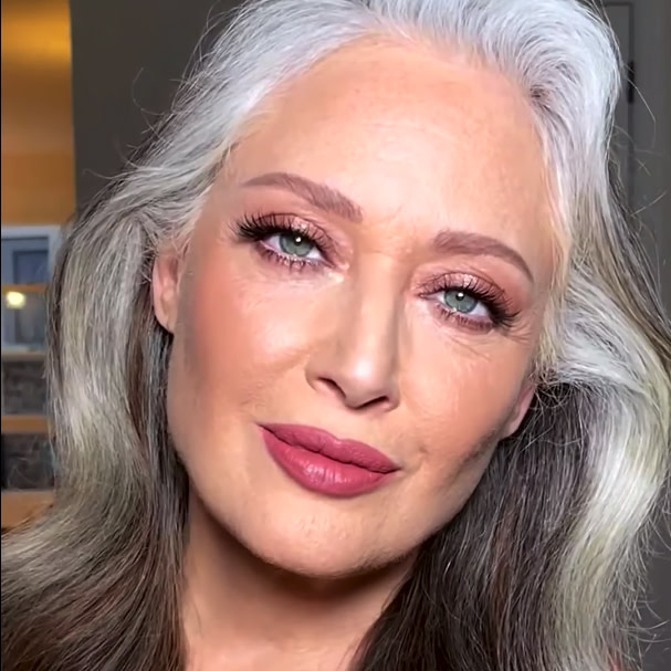 A fair-tone model with mature skin and blue eyes wearing glowy, fresh makeup with berry-pink lipstick and subtle shimmery eyeshadow, which is a  perfect makeup look for the mother of the bride.