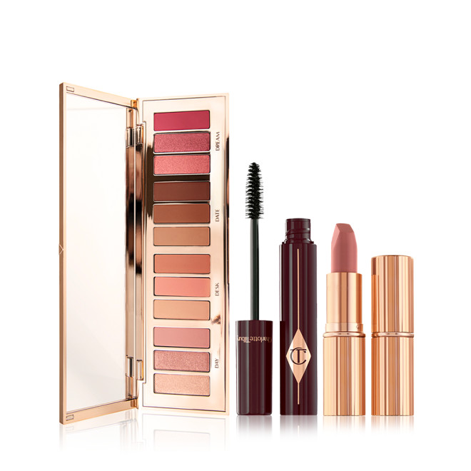 An open, mirrored-lid eyeshadow palette with nude pink, peach, and brown shades, an open mascara with its applicator next to it, and an open nude pink lipstick with a closed lipstick. 