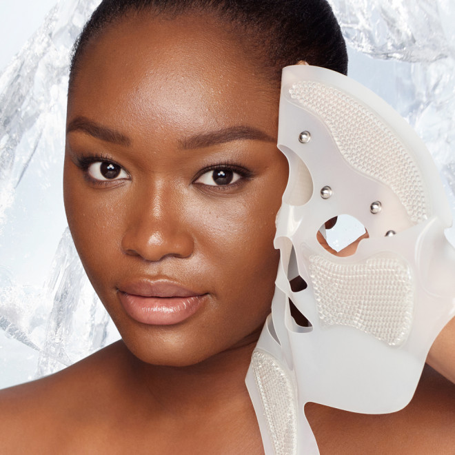 Deep-tone brunette model removing a reusable, white-coloured mask, revealing glowy, flawless, and lifted skin. 