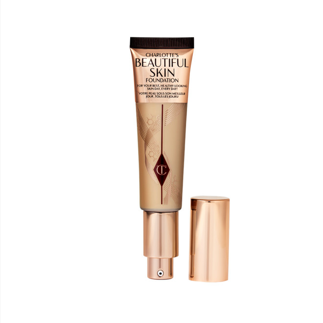 An open foundation wand in gold packaging with a pump dispenser and a medium-brown-coloured body to show the shade of the foundation inside. 
