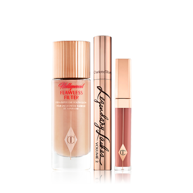 Charlotte's Hollywood Secrets Makeup kit displayed Luminous, dark beige-coloured primer in a glass bottle with gold-coloured lid, mascara in gold-coloured tube and lid, and liquid lipstick in a nude pinky brown colour.
