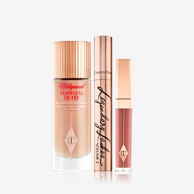 Charlotte's Hollywood Secrets Makeup kit displayed Luminous, dark beige-coloured primer in a glass bottle with gold-coloured lid, mascara in gold-coloured tube and lid, and liquid lipstick in a nude pinky brown colour.