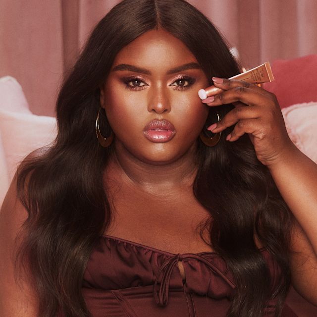 Beauty Light Wand in Pillow Talk Medium on deep-tone model Deep-tone brunette model wearing glowy, nude pink, full-glam makeup and applying pink-peach liquid highlighter-blush from a highlighter blush wand with a soft-sponge applicator end.