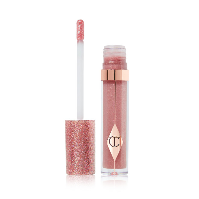 An open, nude-pink lip gloss in a glass tube with its shimmery, rose gold lid placed next to it.