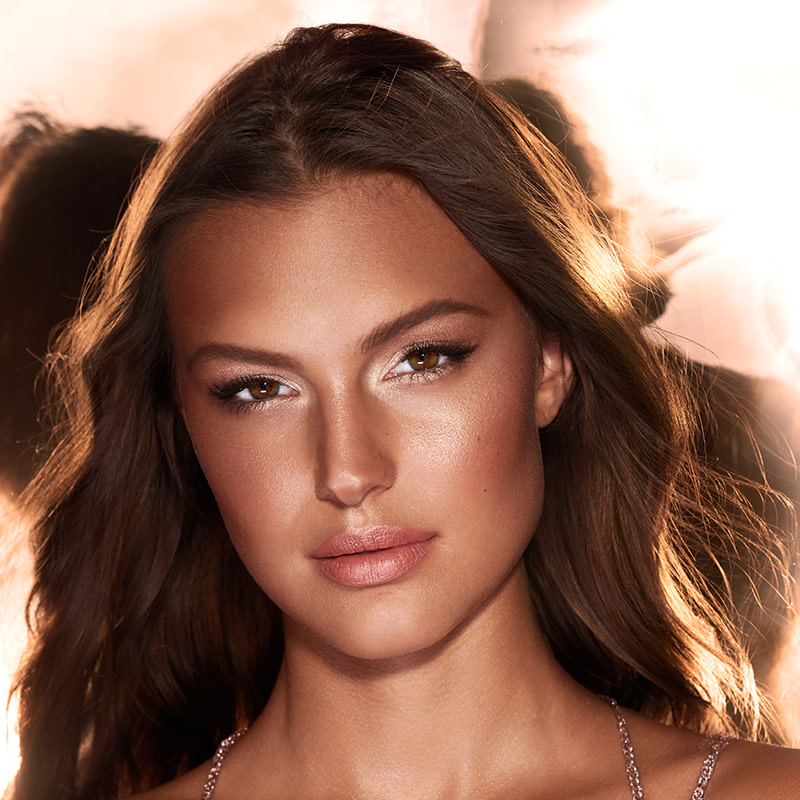 Medium-toned, brunette model with extremely glowy bronze face makeup.