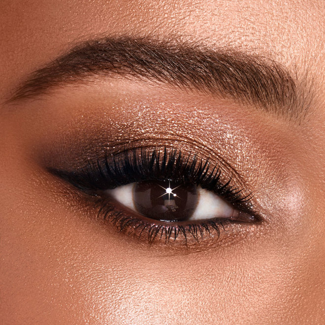 Single-eye close-up of a medium-tone model with brown eyes wearing shimmery gold and brown eyeshadow. 