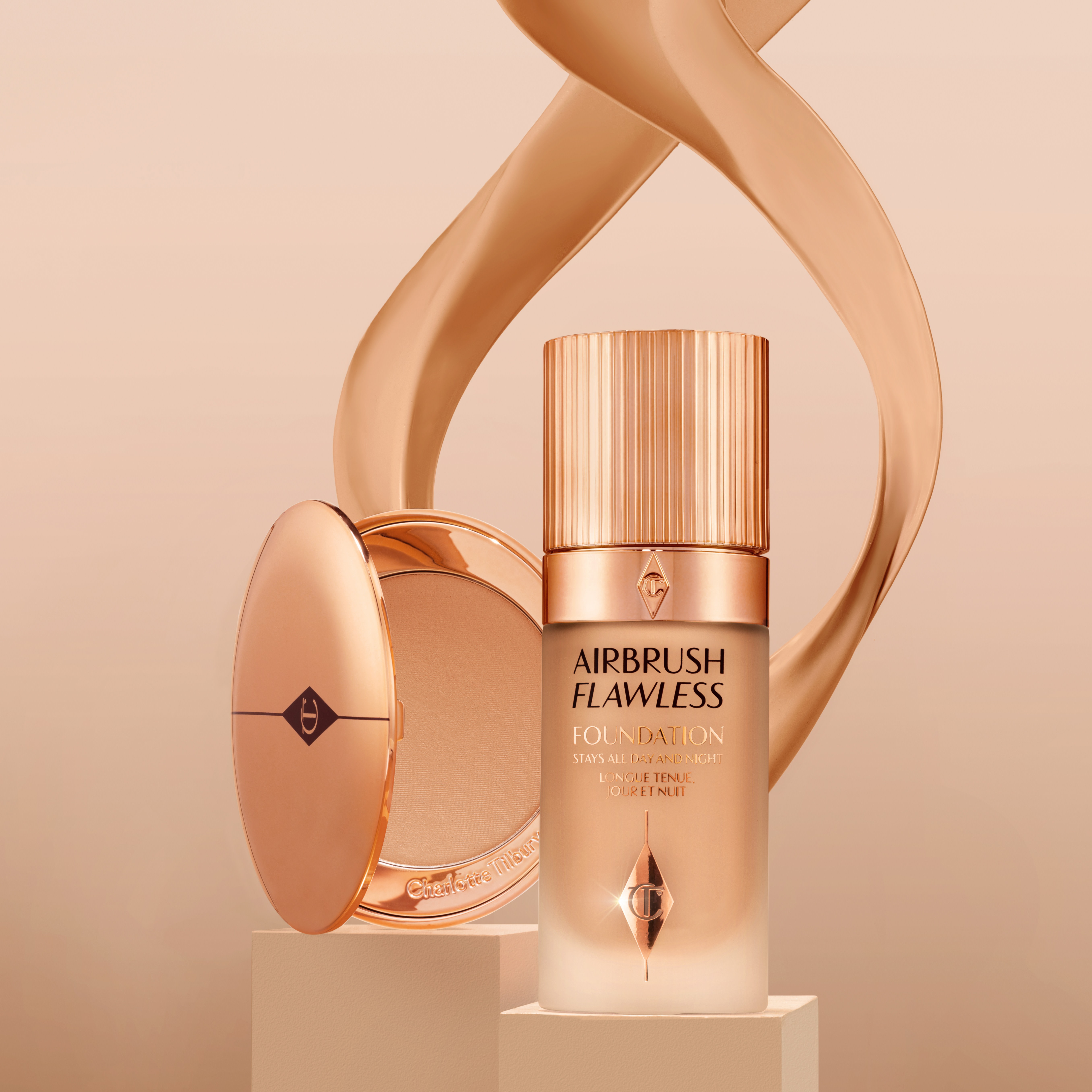 Foundation in a frosted glass bottle with a gold-coloured lid and an open pressed powder compact in gold-coloured packaging 