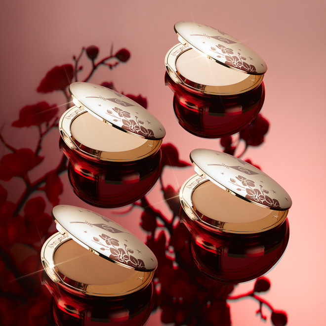 Collection of open, pressed powder compacts for fair, tan light, and deep skin tones with mirrored lids, in gold-coloured packaging with red-coloured tiger stripes on the lids.