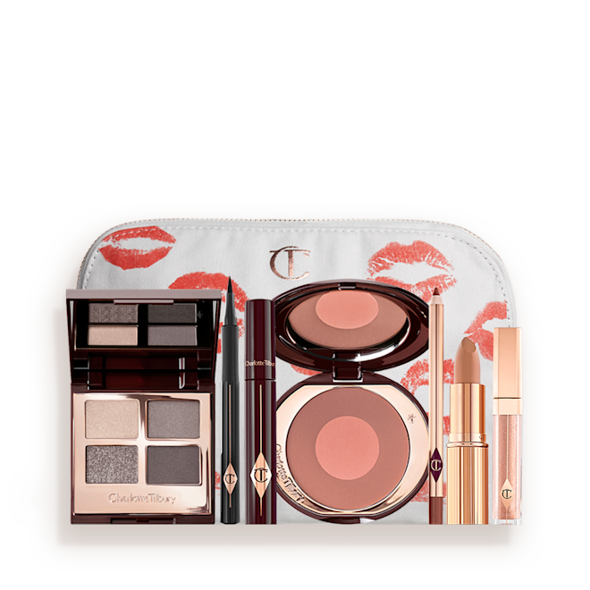 The Rock Chick deep Look kit displayed with makeup pouch A white-coloured makeup pouch with an open two-tone blush in cool-toned brown and rose gold with a mascara, eyeliner pen, quad eyeshadow palette with shimmery and matte grey, beige and silver shades, an open lipstick in nude red, lip liner pencil in taupe-brown, and a lip gloss in nude pink.