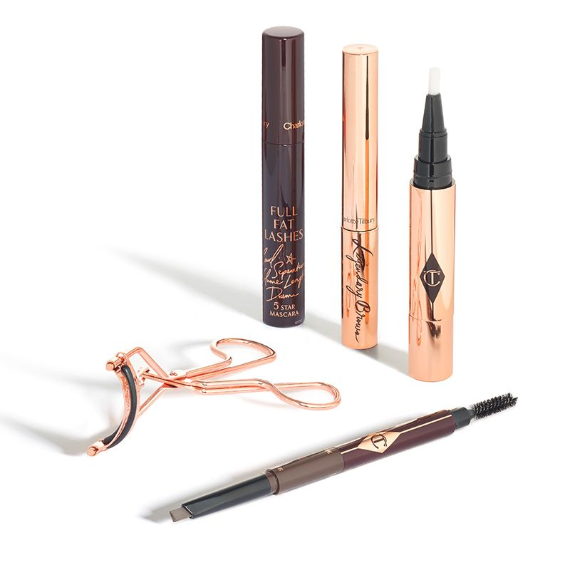 A rose-gold-coloured eyelash curler with a double-sided eyebrow brush and tint, two mascaras, and an open undereye concealer. 
