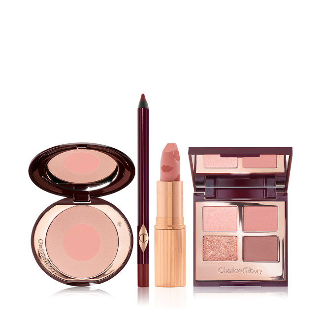 An open, two-tone blush compact in nude pink and champagne, eyeliner in berry-brown, open lipstick in muted pink, and quad eyeshadow palette with matte and shimmery shades of pink, gold, and brown with a mirrored-lid.