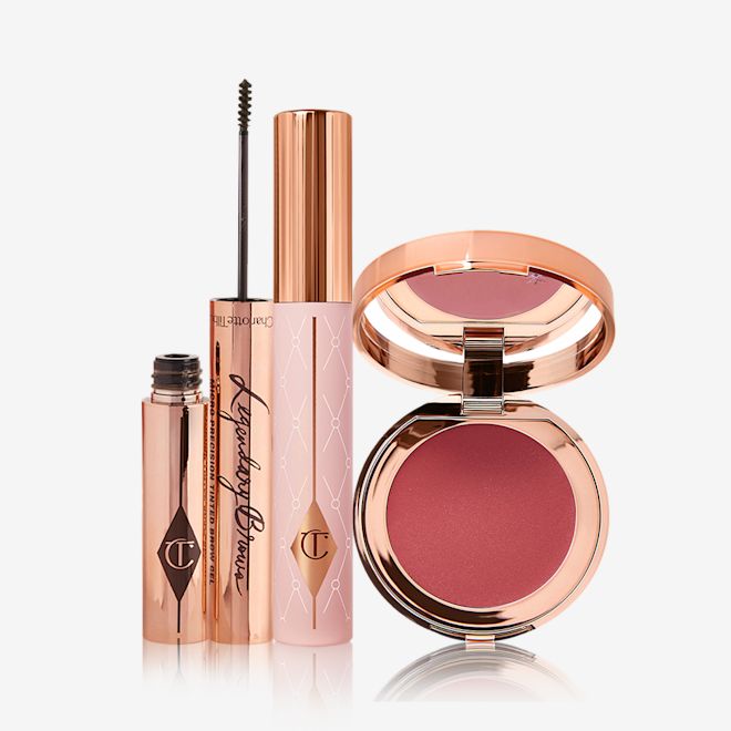 Pillow Talk Lash Brow Glow Kit displayed An eyebrow tint with its thin applicator for precise application next to it, mascara in a nude pink-coloured tube with a gold-coloured lid, and a lip and cheek tint compact with a mirrored-lid in a berry-rose shade.
