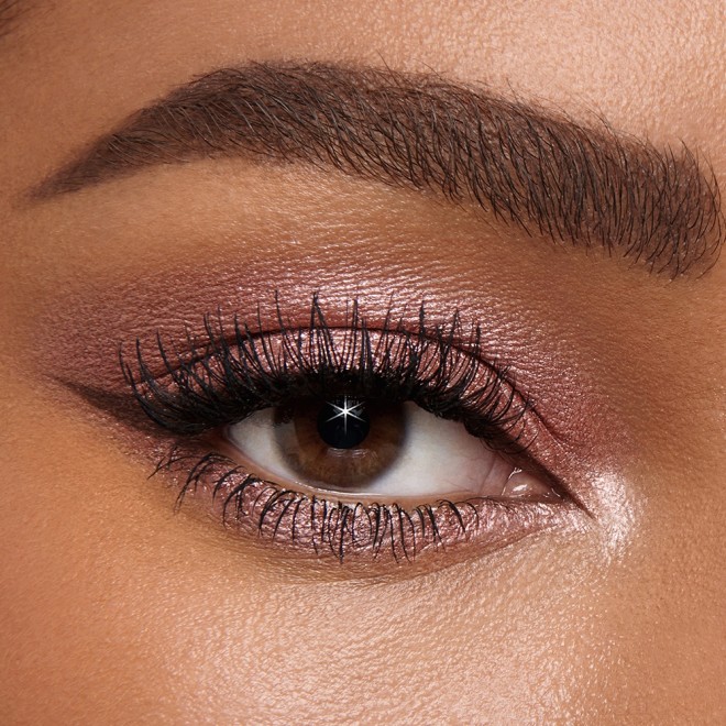 Single-eye close-up of a deep-tone model with brown eyes wearing shimmery rose gold eyeshadow with black eyeliner. 