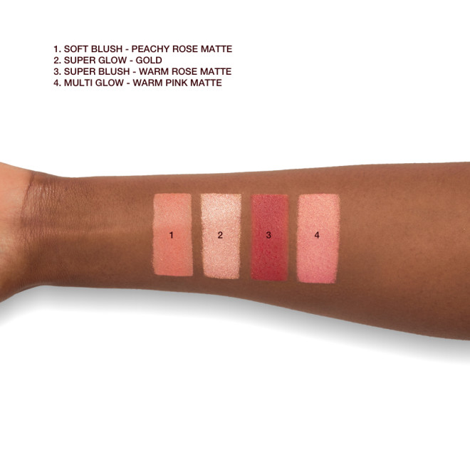 A deep-tone model's arm with swatches of an eyeshadow, highlighter, and two blushes in shades of copper-pink, candlelight gold, medium pink, and berry-pink.