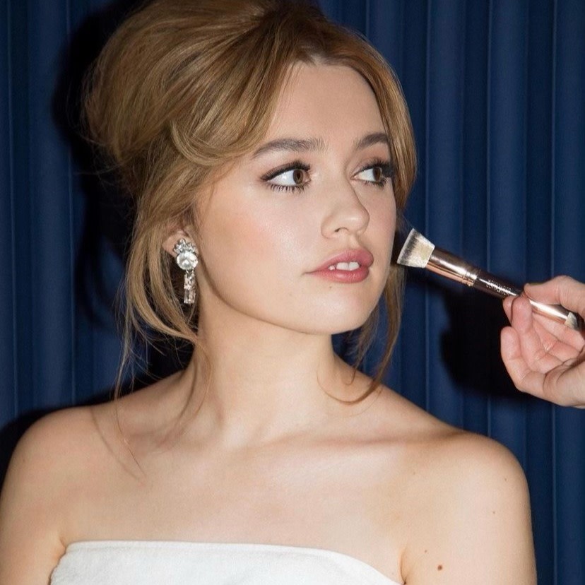 Actress, Aimee Lou Wood, wearing a strapless white dress and getting her makeup done at the BAFTAs 2021 awards ceremony.