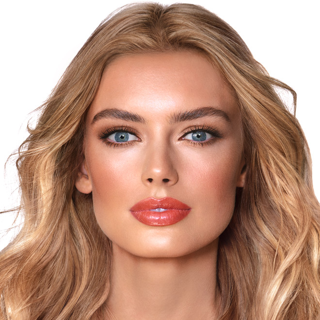 A light-tone model with blue eyes wearing smokey brown eye makeup with warm bronze and pink blush, and glossy terracotta lips.