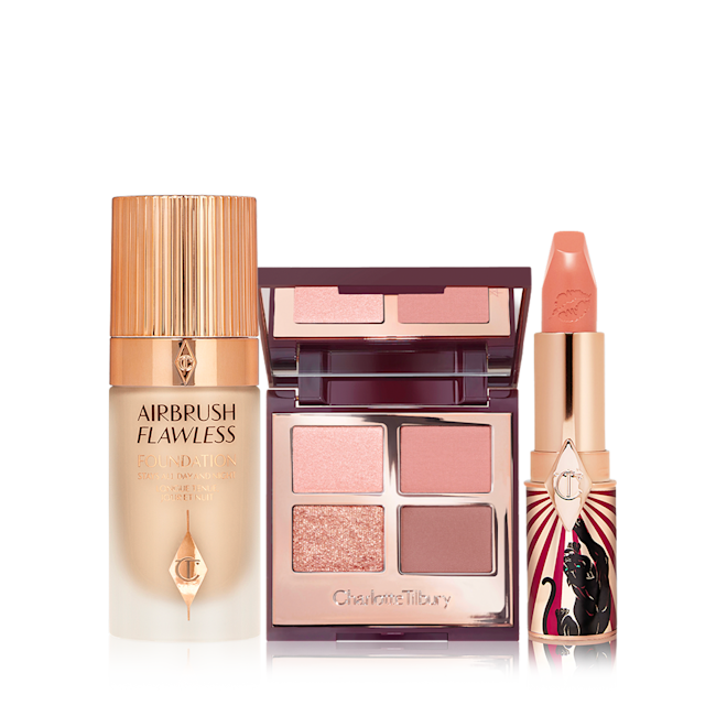 Charlotte's Makeup Magic Kit displayed Foundation in a glass bottle with gold-coloured lid, open mirrored-lid quad eyeshadow palette with an open, nude peach lipstick in a funky tube with a panther on it.