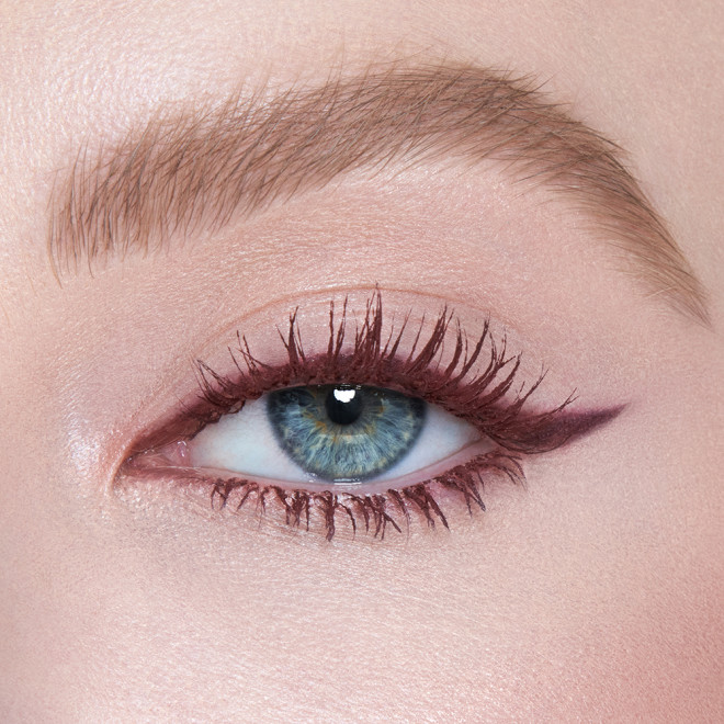 Single-eye close-up of a fair-tone model with blue eyes wearing a berry-brown, lengthening mascara that gives her lashes the appearance of false lashes.