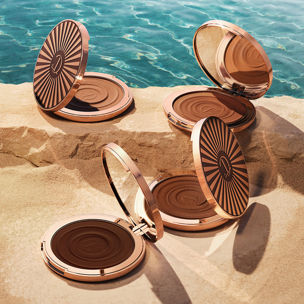 Beautiful Skin Sun-Kissed Glow Bronzer collection open Four, open cream bronzer compacts with mirrored lids in light brown, medium brown, dark brown, and black-brown shades with gold-coloured bodies and lids.