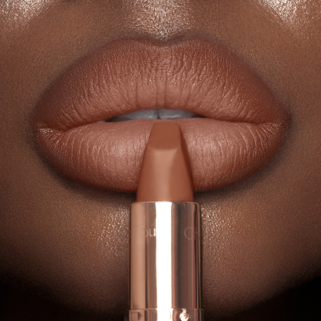 Lips close-up of a deep-tone model wearing a fresh, neutral nude peach lipstick with a matte finish.