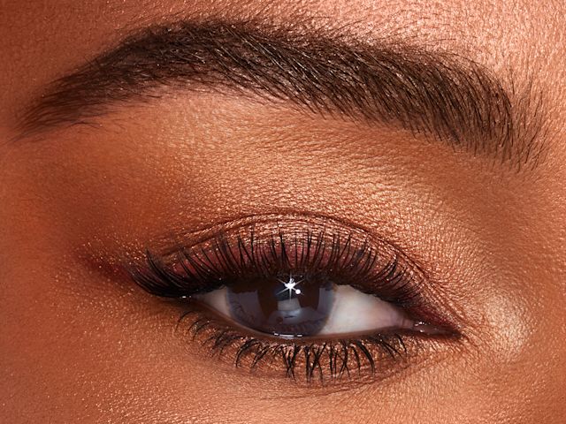 Bejewelled Eyes Happy Glow shades on brown eye close-up Single-eye close-up of a deep-tone model with brown eyes wearing shimmery topaz and brown eyeshadow with dark brown eyeliner pencil.