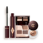 BIGGER BRIGHTER EYE TRICKS An open, mirrored-lid quad eyeshadow palette with beige, brown-gold, rose gold, and dusky pink shades, a mascara in black, and cream eyeshadow in a coppery-gold shade in a glass pot with a dark brown-coloured lid.