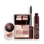 Kit Bigger Brighter Eye Tricks abierto Un cuarteto de sombras de ojos, abierto y con tapa de espejo, con tonos beige, castaño dorado, oro rosado y rosa oscuro, una máscara de pestañas en negro y una sombra de ojos en crema en un tono cobrizo dorado, en un frasco de vidrio con tapa de color castaño oscuro.
