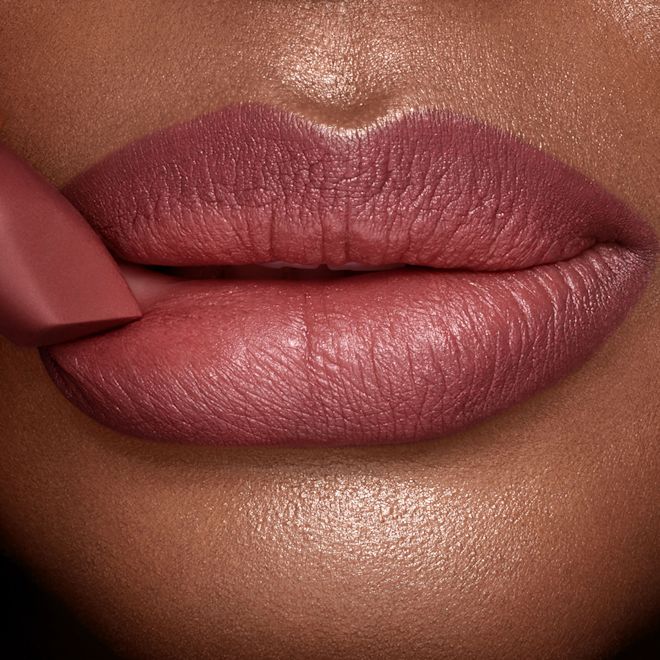 Matte Revolution Pillow Talk Medium lipstick deep tone close-up A deep tone model with glowing skin wearing a berry-pink lipstick with the lipstick gently pressed to the lower lip.