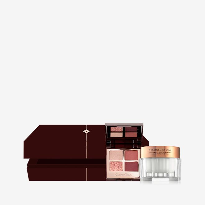 Beauty Secrets Mystery Box open An open, dark brown mystery gift box with an open, quad eyeshadow palette with a mirrored lid with eyeshadows in shades of russet rose, dark brown, rose gold, and dull gold along with a white-coloured face cream in a glass jar with a gold lid next to it.
