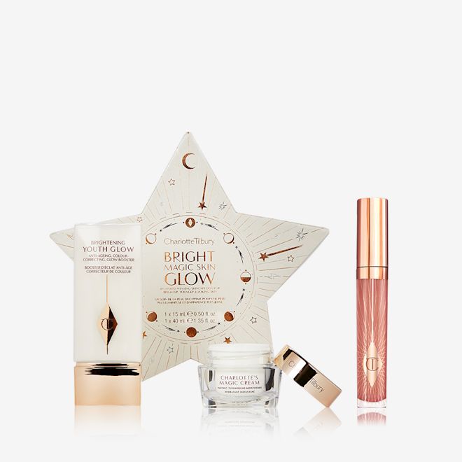 Glowing Skin and Plumper Looking Lips Kit dispalyed Primer in a rectangular glowy bottle with gold-coloured lid, pearly-white face cream in a glass jar with gold-coloured lid, and nude pink lip gloss along with a star-shaped, white-coloured packaging box.