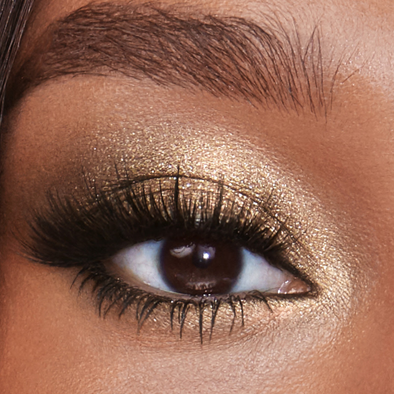 Eye close-up of a single brown eye of a deep-tone model wearing shimmery golden-coloured eyeshadow.