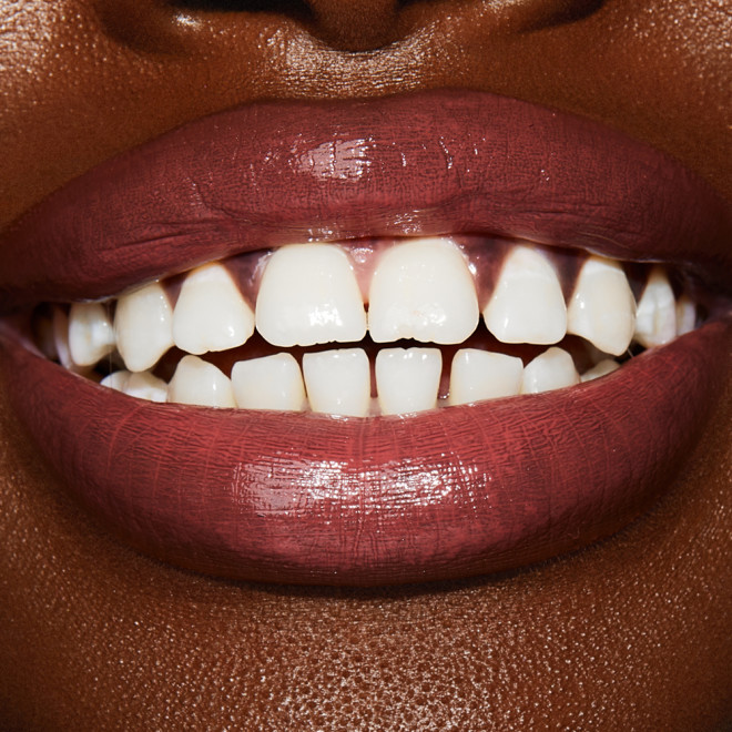 Lips close-up of a deep-tone model wearing a moisturising lipstick balm in a soft pink shade with a high-shine finish.