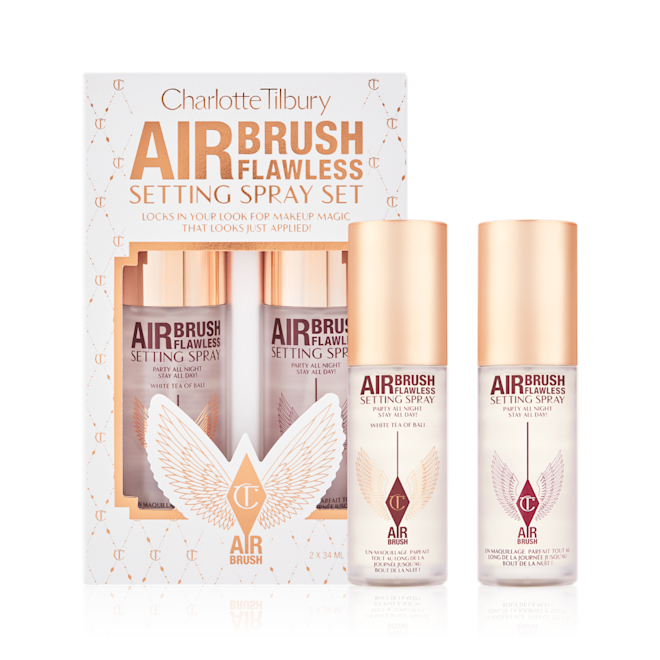Airbrush Flawless Setting Spray Duo with box Two, identical, mini setting sprays with gold-coloured lids and their white and gold-coloured packaging box behind them with gold stars printed all over with text on the box that reads, 'Charlotte Tilbury. Airbrush Flawless Setting Spray Set'