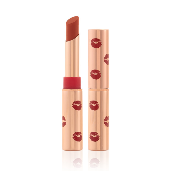 Two matte lipsticks, with and without lids, in gold-coloured tubes with kiss prints all over in tawny orange-red  colour.
