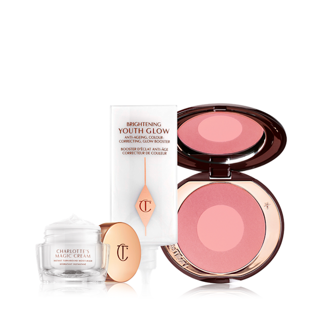 Glowing Skin Blushed Cheeks Kit An open glass pot filled with pearly-white face cream, glowy primer in a white-coloured tube, and a two-tone glowy blush in medium pink and pearlescent pink.