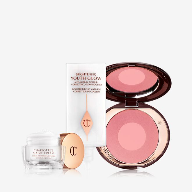 Glowing Skin Blushed Cheeks Kit An open glass pot filled with pearly-white face cream, glowy primer in a white-coloured tube, and a two-tone glowy blush in medium pink and pearlescent pink.