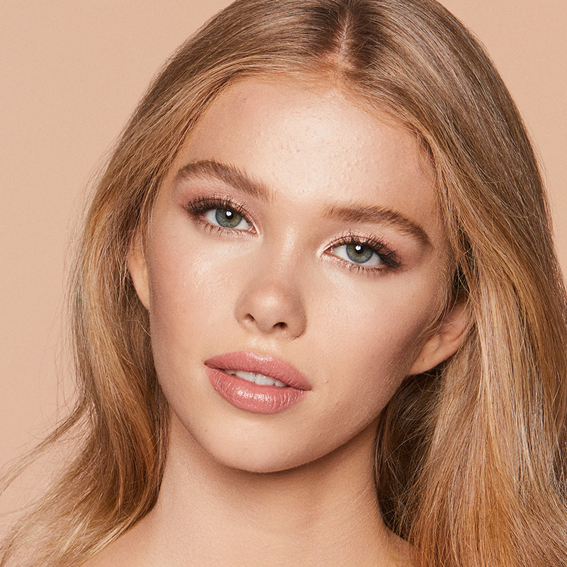 A fair-tone blonde model with blue eyes wearing dewy, nude pink makeup. 