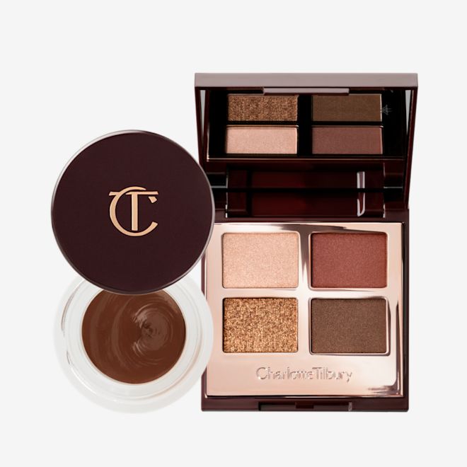 Charlotte's Smokey Eye Duo open An open eyeshadow pot with a dark, chocolate-brown cream shadow with a matte finish inside with its lid next to it, and an open quad eyeshadow palette with a mirrored-lid with matte and shimmery eyeshadows in shades of gold, brown, and champagne.