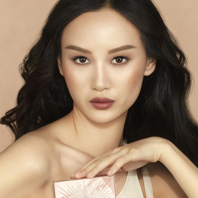 Fair-tone brunette model wearing glowy peach blush with heavily contoured cheekbones, smokey brown eye makeup, and subtle highlighter with berry nude lipstick.