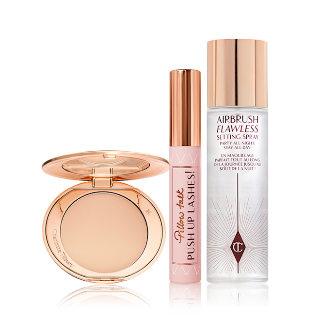 Airbrush Skin Pillow Talk Lashes kit displayed Setting powder compact with a mirrored-lid in sleek, gold packaging, mascara in a nude pink tube with a gold-coloured lid, and setting spray in a large bottle with a gold-coloured lid.