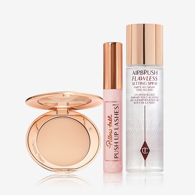 Airbrush Skin Pillow Talk Lashes kit displayed Setting powder compact with a mirrored-lid in sleek, gold packaging, mascara in a nude pink tube with a gold-coloured lid, and setting spray in a large bottle with a gold-coloured lid.