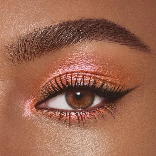 Single-eye close-up of a deep-tone model with brown eyes wearing golden pink duo-chrome-effect cream eyeshadow with a duo-chrome metallic finish,