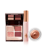 An open, quad eyeshadow palette with a mirrored-lid in red, pink, and gold shades, mascara in a nude pink tube with a gold-coloured lid, and cream eyeshadow in a glass pot in a coppery-gold shade.