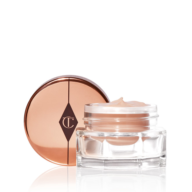 An open, light champagne-coloured eye cream in a glass pot with its rose-gold-coloured lid next to it. 