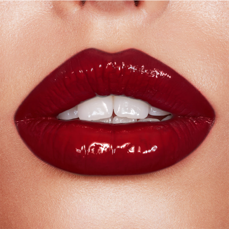 Lips close-up of a fair-tone model wearing a vivid, opaque, crimson-red lip gloss. 